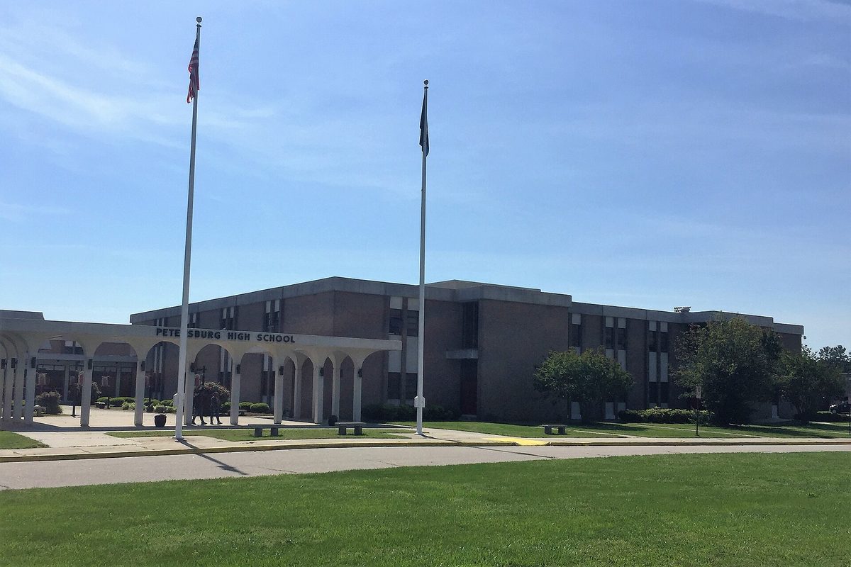 Petersburg High School, a low brick building with an arched entry walkway, two flagpoles and a wide green lawn