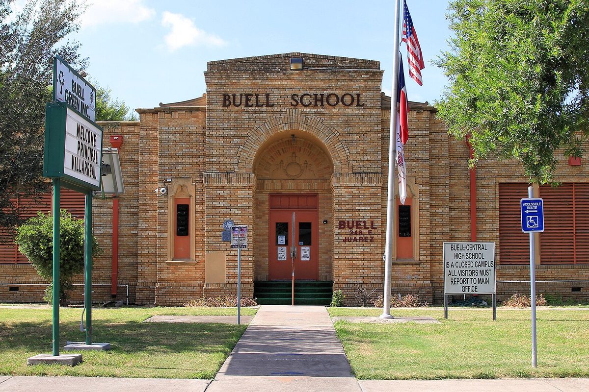 The historic brick Buell School in Pharr, with an arched doorway, a flagpole with American and Texas flags, a green school sign and a campus notice on the lawn