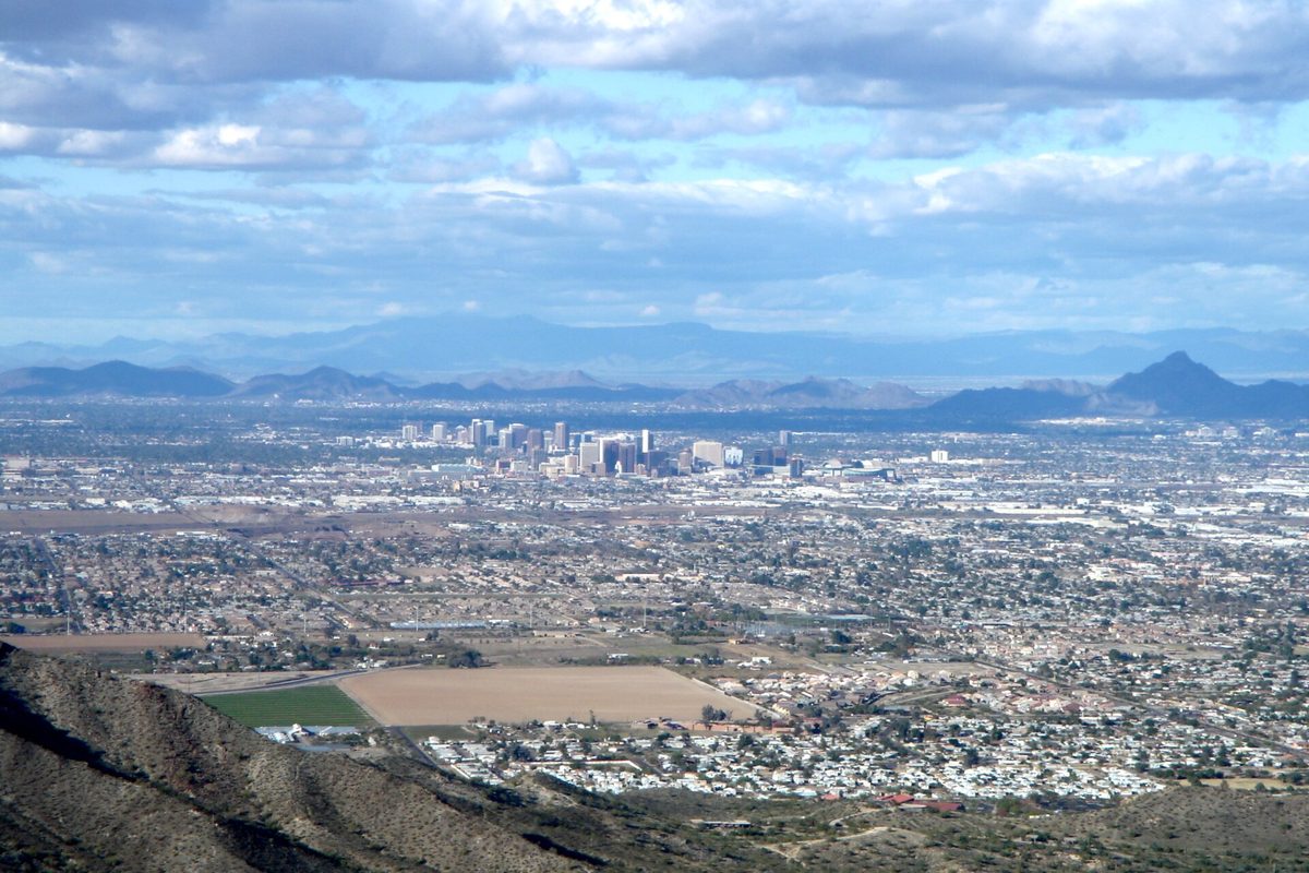 Downtown Phoenix towers rising from the wide, flat city, with mountain ranges and clouds beyond, seen from South Mountain