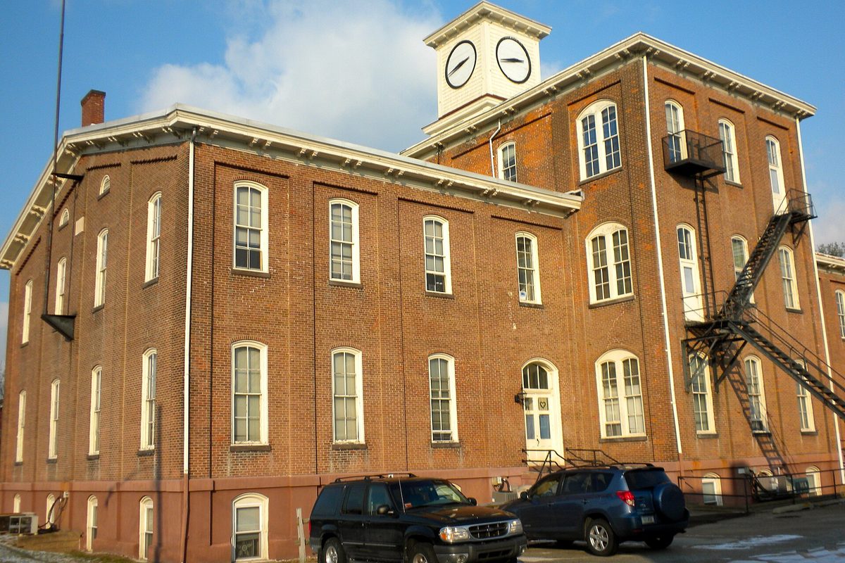 The three-story brick Gay Street School in Phoenixville, with a white clock tower, tall arched windows and a black fire escape, two SUVs parked in front