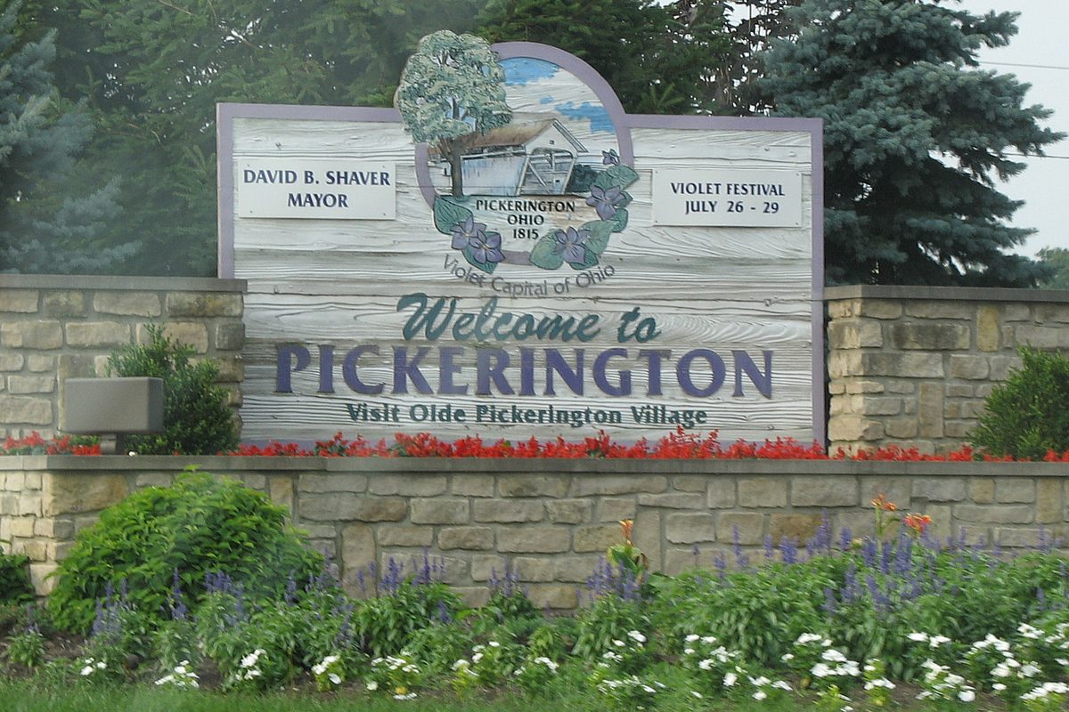 Stone-walled Welcome to Pickerington sign calling the city the Violet Capital of Ohio, with red flowers along its base and a flower bed in front