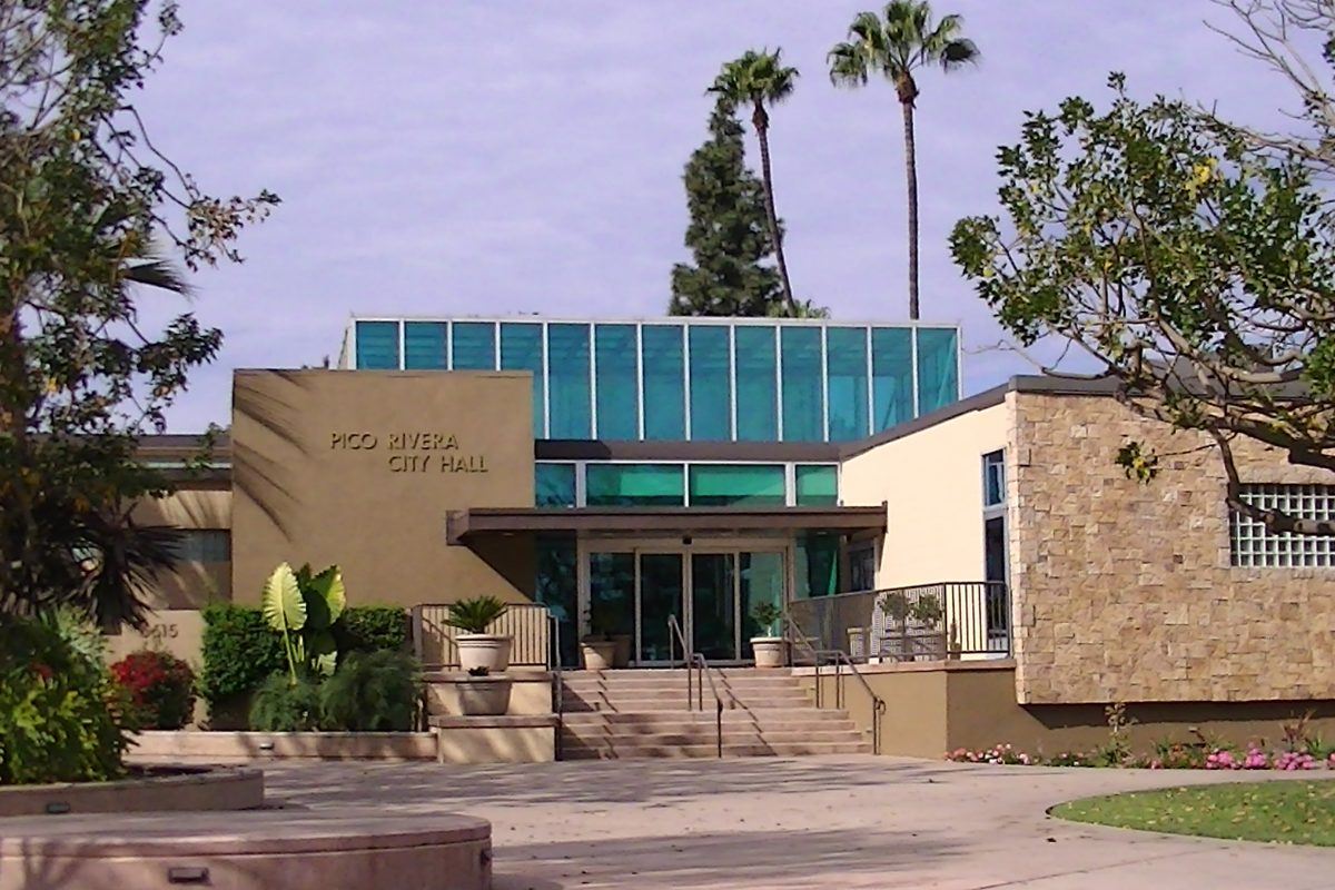 Front steps and the teal glass upper floor of Pico Rivera City Hall, framed by palm trees and garden plants