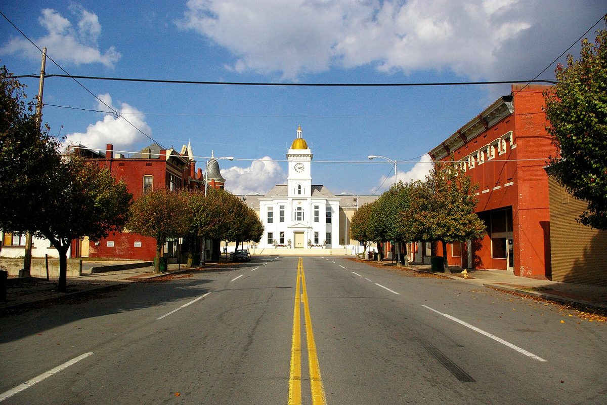 Main Street in Pine Bluff, lined with red-brick storefronts and trees, leading to the white Jefferson County Courthouse with its gold-domed clock tower