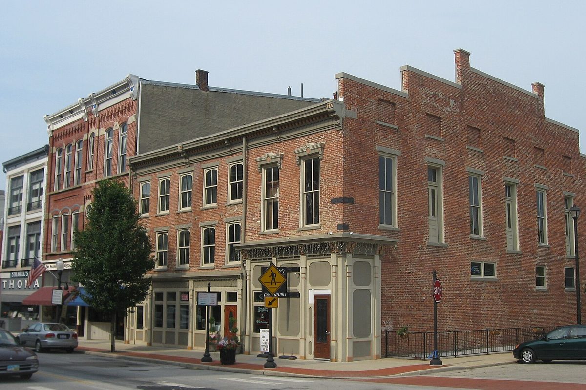 Two- and three-story brick storefronts on North Main Street in downtown Piqua, with a pedestrian crossing sign and a stop sign at the corner