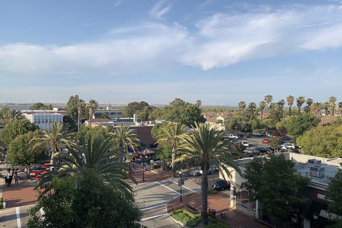 Old Town Pittsburg from above: palm trees, a brick plaza and low buildings along Railroad Avenue, with wind turbines on the far hills