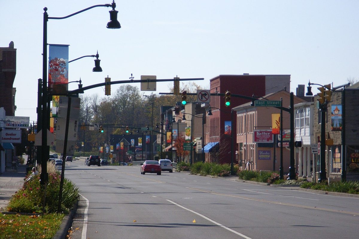 Downtown Plainfield's main road lined with lamp posts, banners and brick storefronts, with autumn trees at the far end