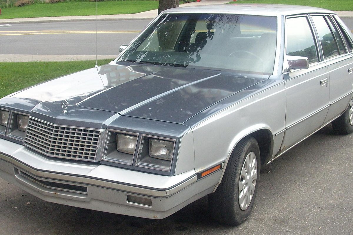 A two-tone silver Plymouth Caravelle four-door sedan with a dark gray hood, parked at a curb on a residential street