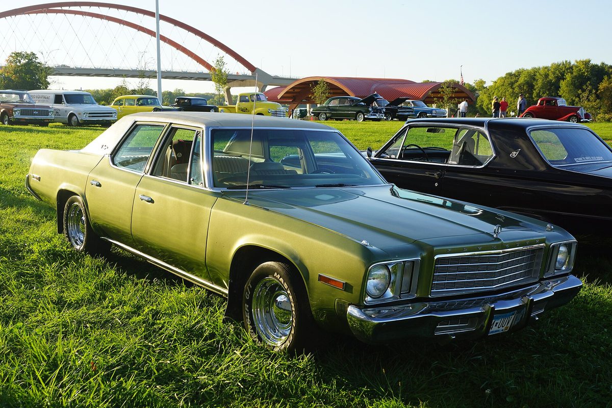 A green Plymouth Gran Fury four-door sedan with chrome bumpers and chrome wheels, parked on grass at a car show