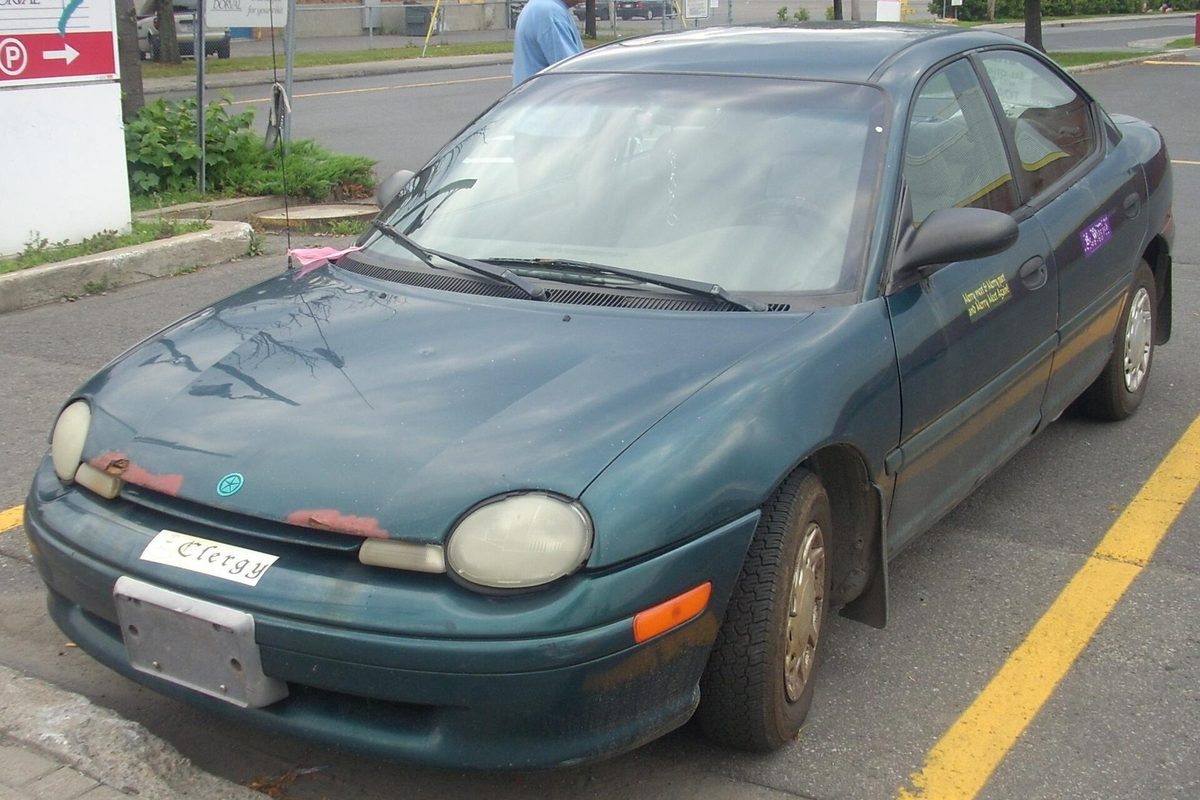 A green 1995 Plymouth Neon sedan with faded, peeling paint on the hood and front bumper, parked in a lot