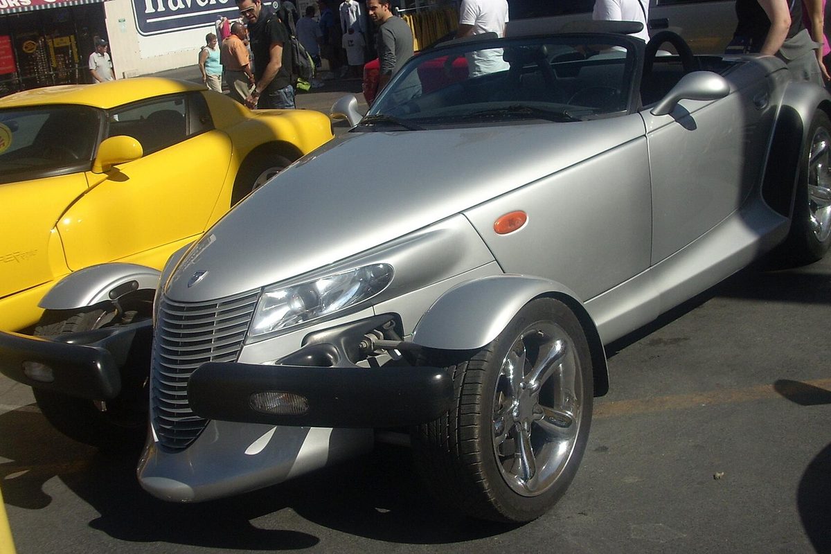 A silver Plymouth Prowler roadster with its top down at a street car show, a yellow Prowler parked beside it