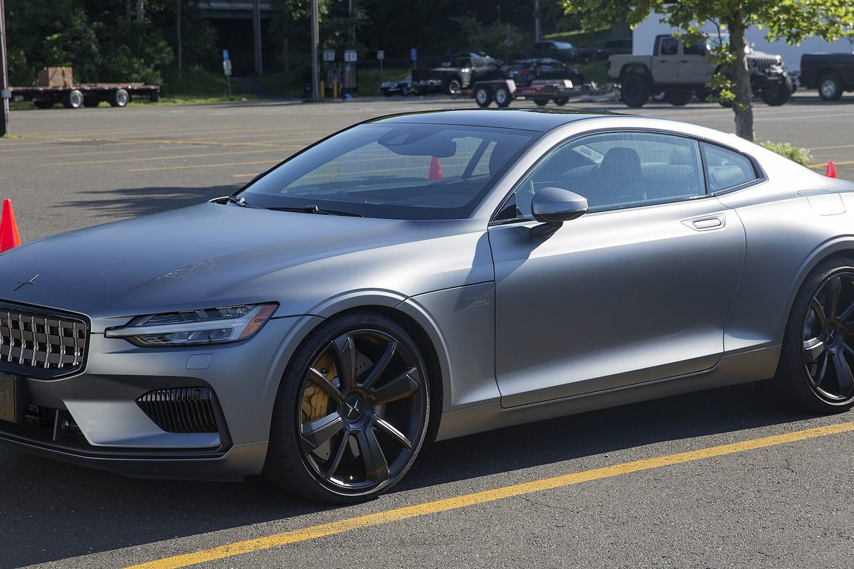 A matte gray Polestar 1 coupe with black wheels and gold brake calipers, parked in a lot beside orange traffic cones
