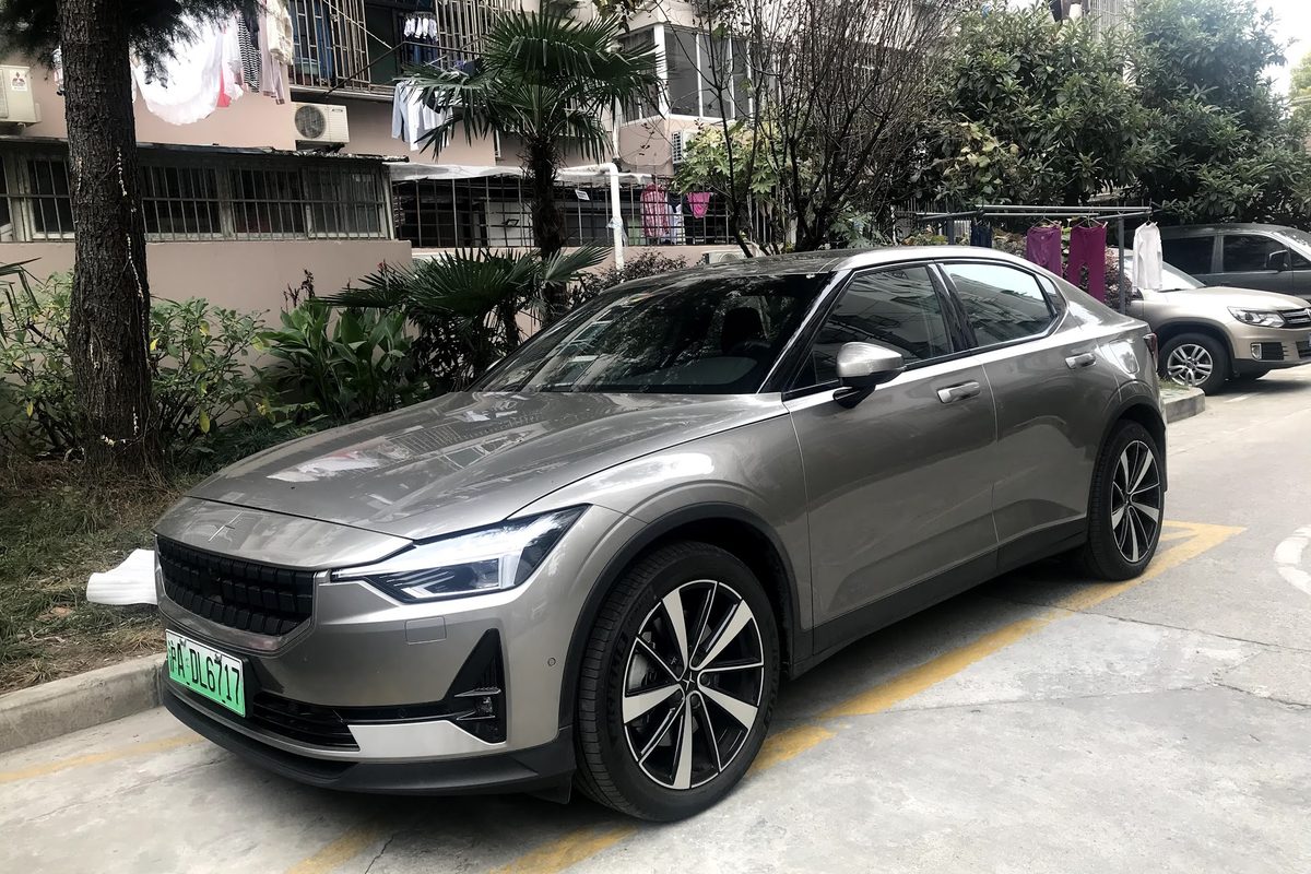 A gray Polestar 2 fastback parked at a curb in front of an apartment block, with laundry hanging from the balconies