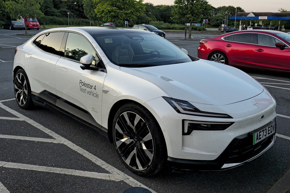 A white Polestar 4 SUV with test vehicle lettering on its rear door, parked in a marked lot at dusk