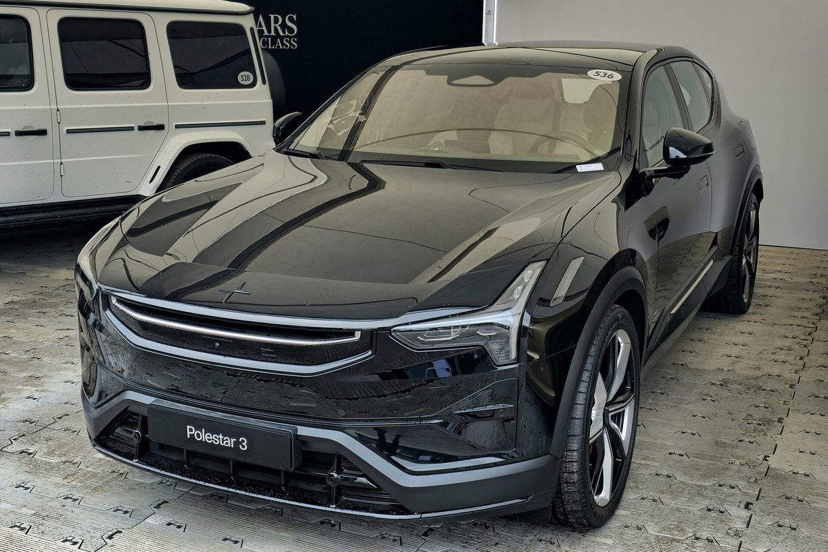 A black Polestar 3 electric SUV parked on a paved display floor, seen from the front left, with a white SUV beside it