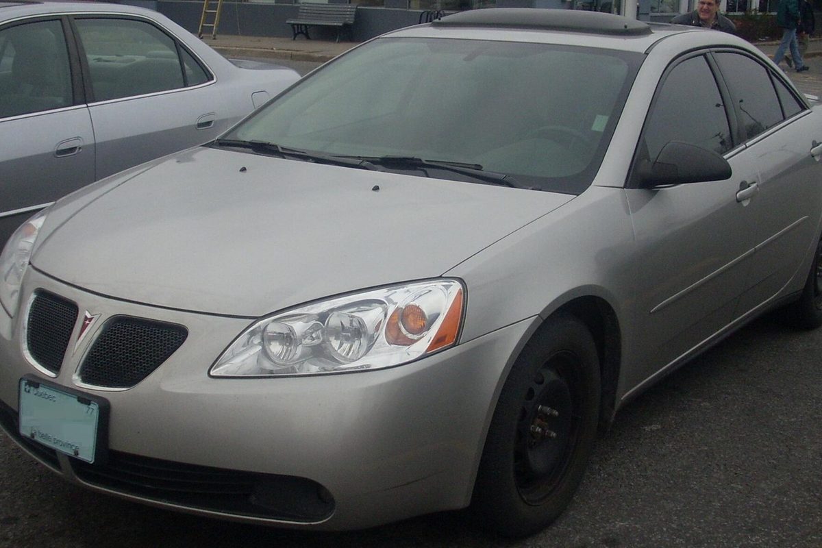 A pale silver-beige Pontiac G6 sedan on plain black steel wheels, parked in a lot beside another sedan