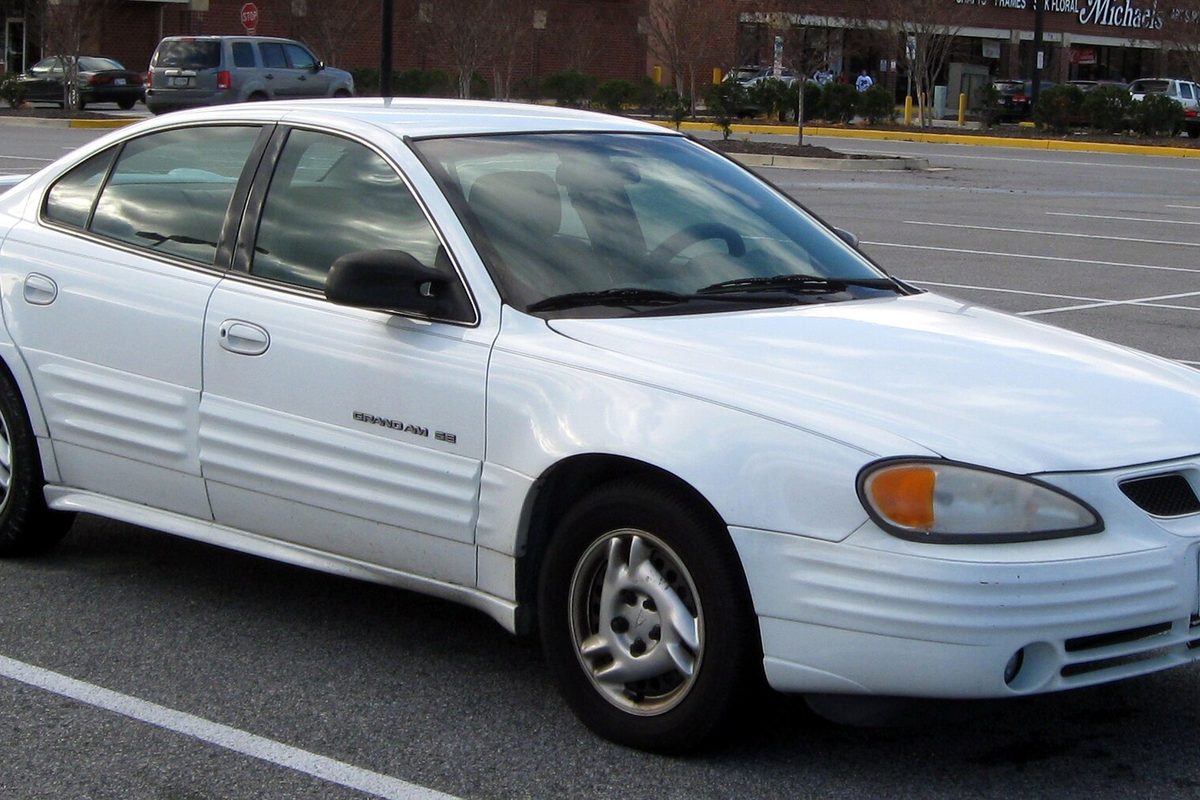 A white fifth-generation Pontiac Grand Am SE sedan with ribbed lower door panels, parked in a store lot