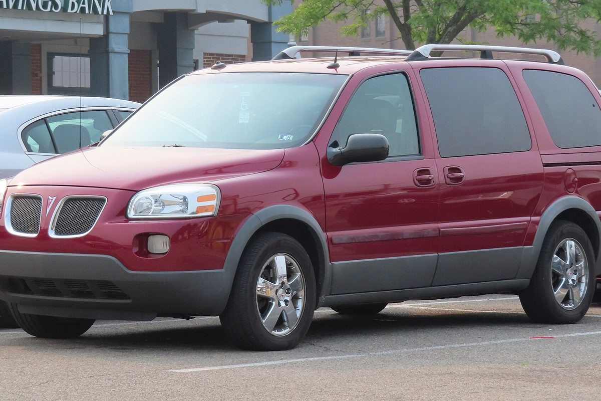 A dark red Pontiac Montana SV6 minivan with roof rails, gray lower cladding and chrome wheels in a parking lot