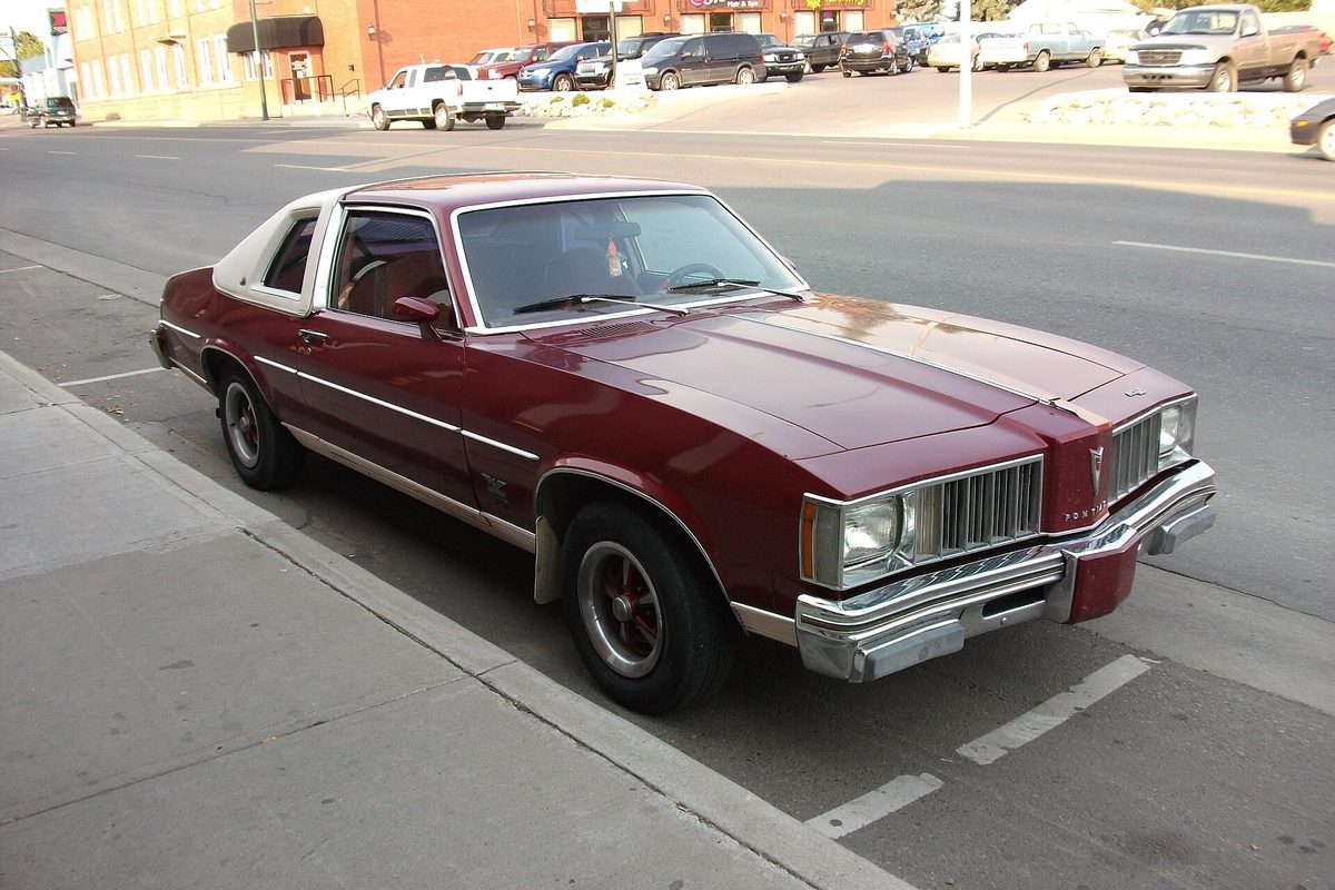 A maroon first-generation Pontiac Phoenix SJ coupe with a white vinyl roof and chrome bumpers, parked at a curb