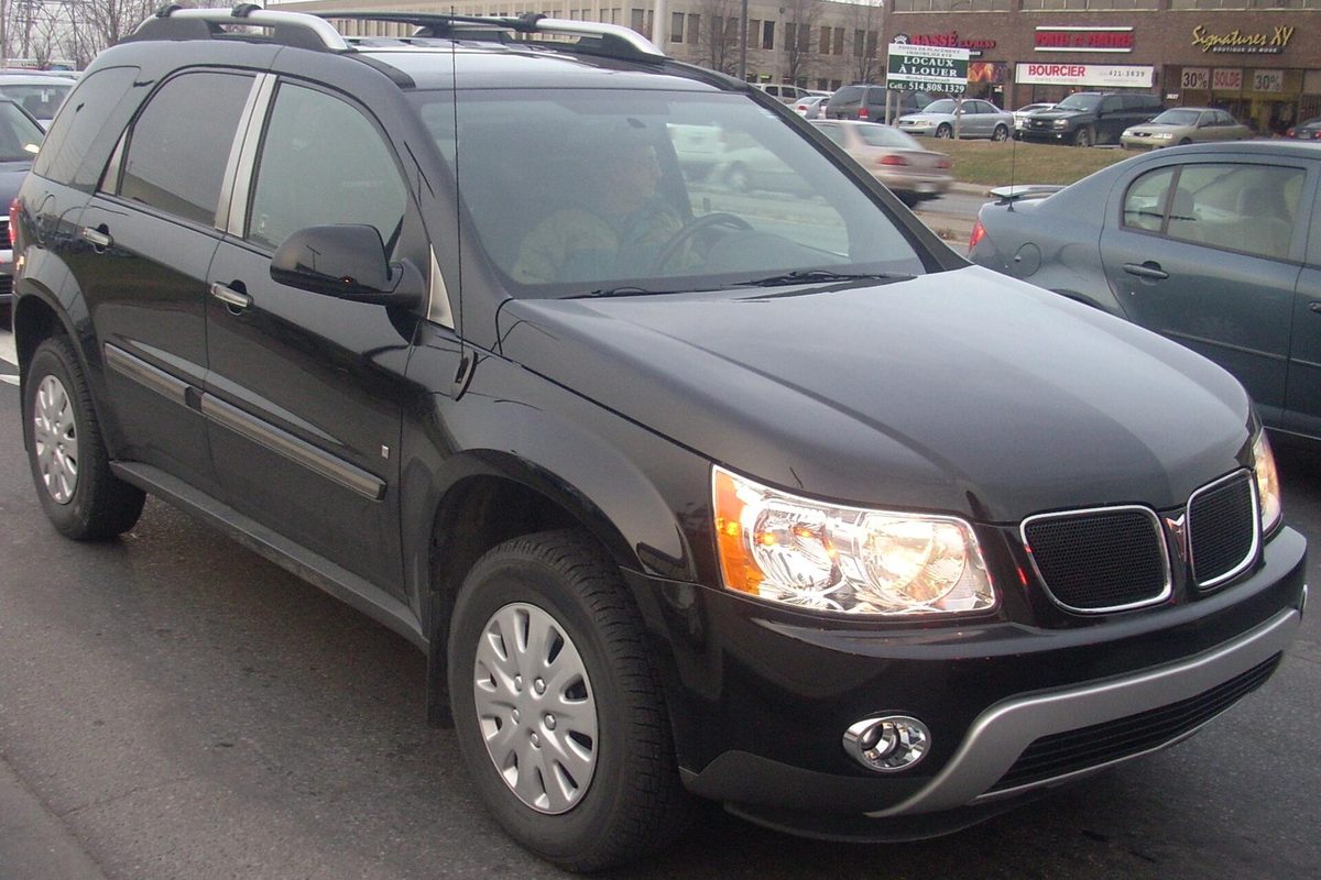 A black Pontiac Torrent crossover with roof rails and silver wheel covers, parked in a shopping-plaza lot