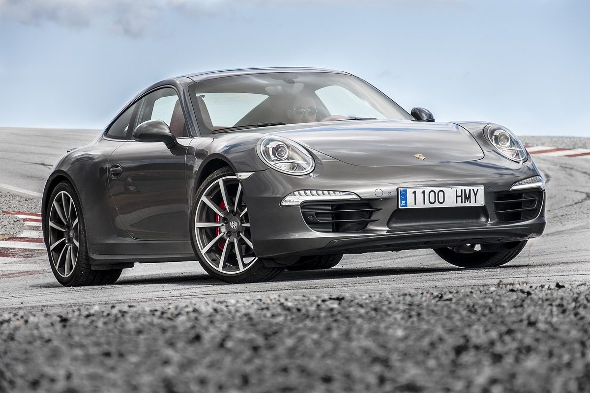 A dark gray 2013 Porsche 911 Carrera 4S coupe on a race track under a cloudy sky
