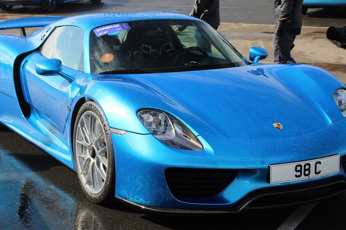 A metallic blue Porsche 918 Spyder parked on wet pavement, seen from the front corner with raindrops beaded on the hood