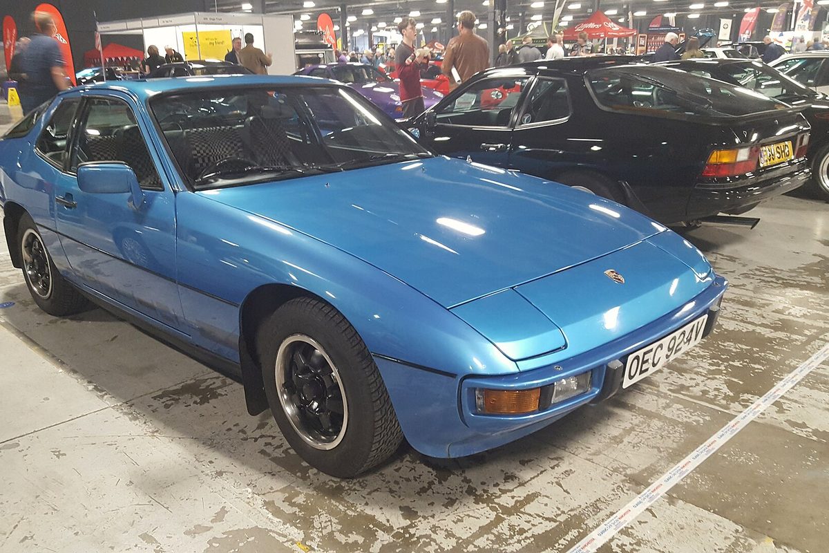 A blue Porsche 924 hatchback coupe with black wheels at an indoor classic car show