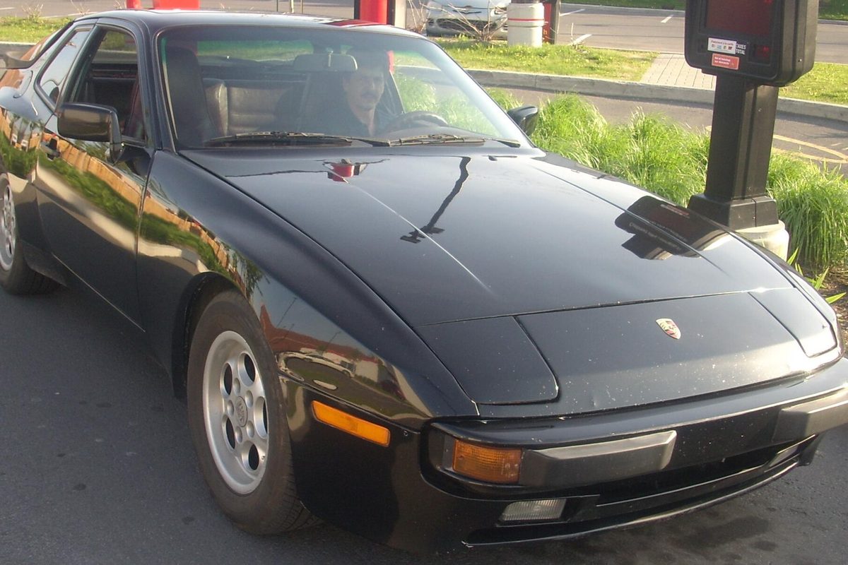 A black Porsche 944 coupe with silver wheels parked beside a gas pump
