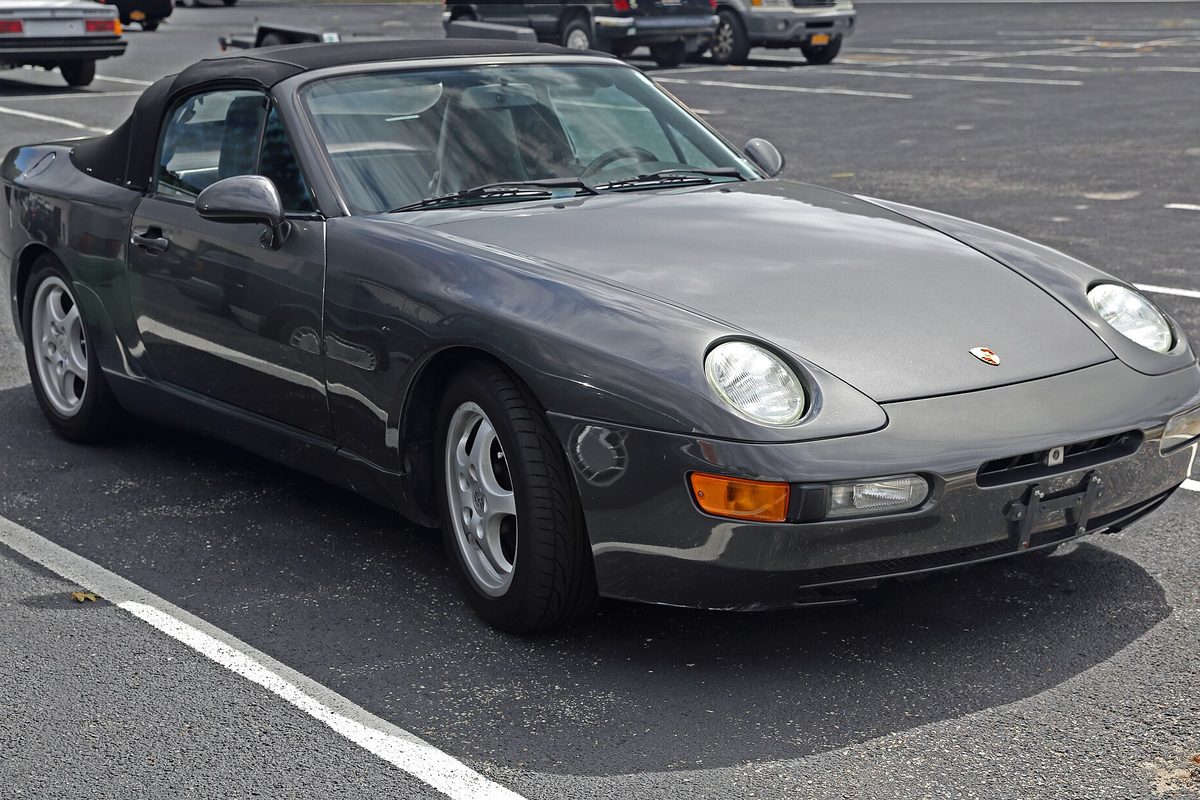 A dark gray Porsche 968 Cabriolet with its black soft top up, parked in an empty lot