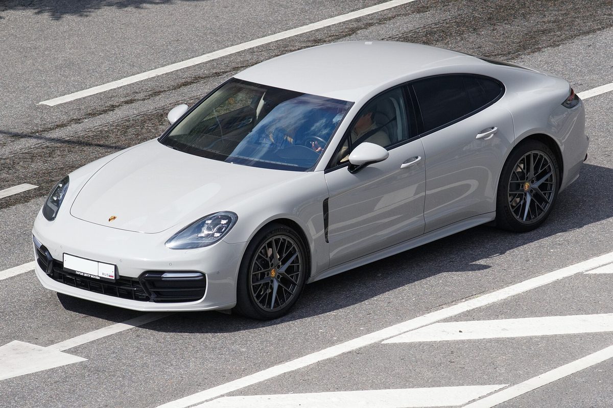 A light gray Porsche Panamera sedan seen from above, driving across white road markings