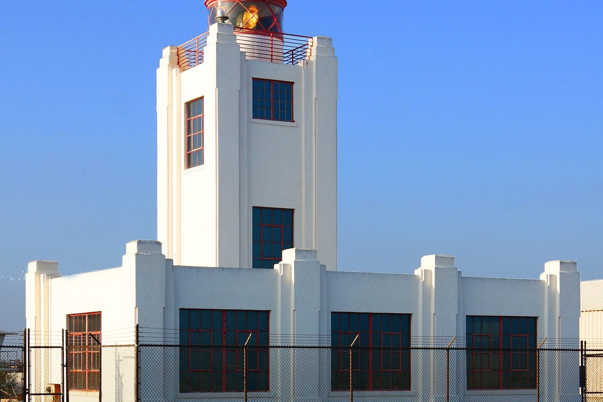 The white Art Deco Point Hueneme Lighthouse with its lantern on top, behind a chain-link fence under a clear blue sky