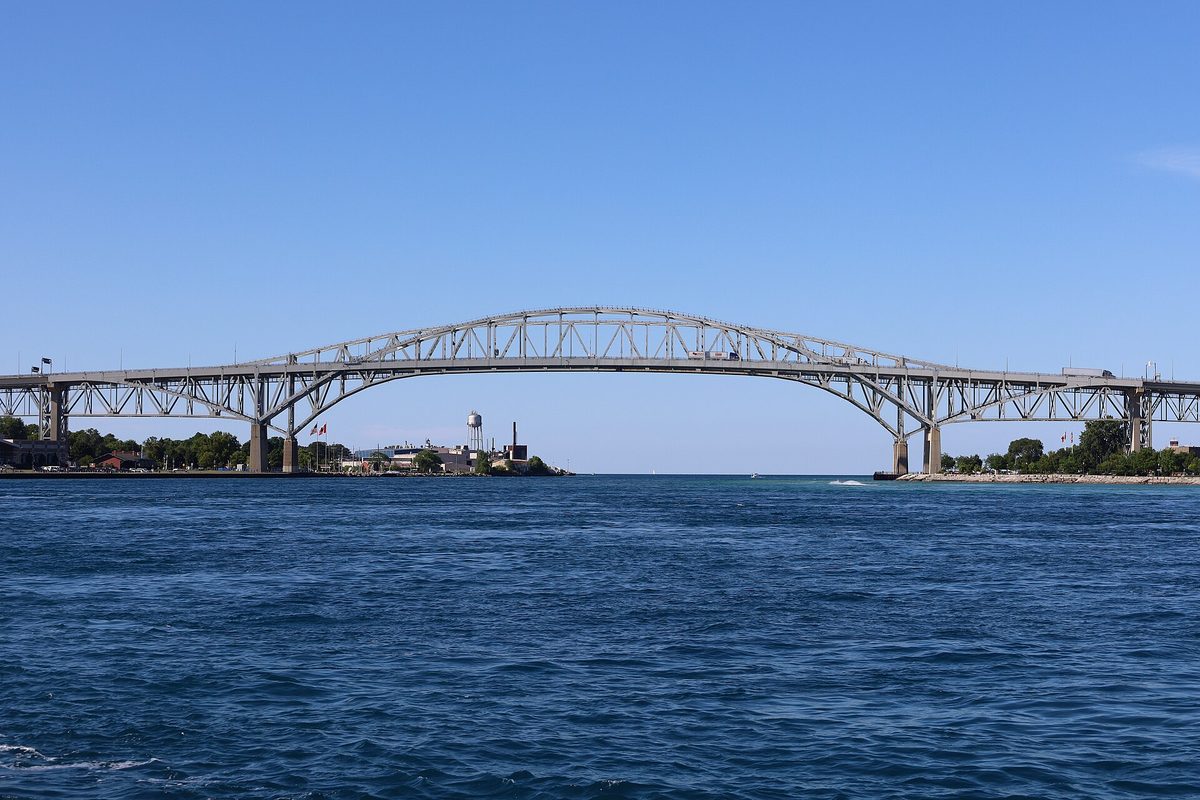 The Blue Water Bridge, two steel arch spans side by side, crossing a wide blue river under a clear sky, with a water tower on the far shore