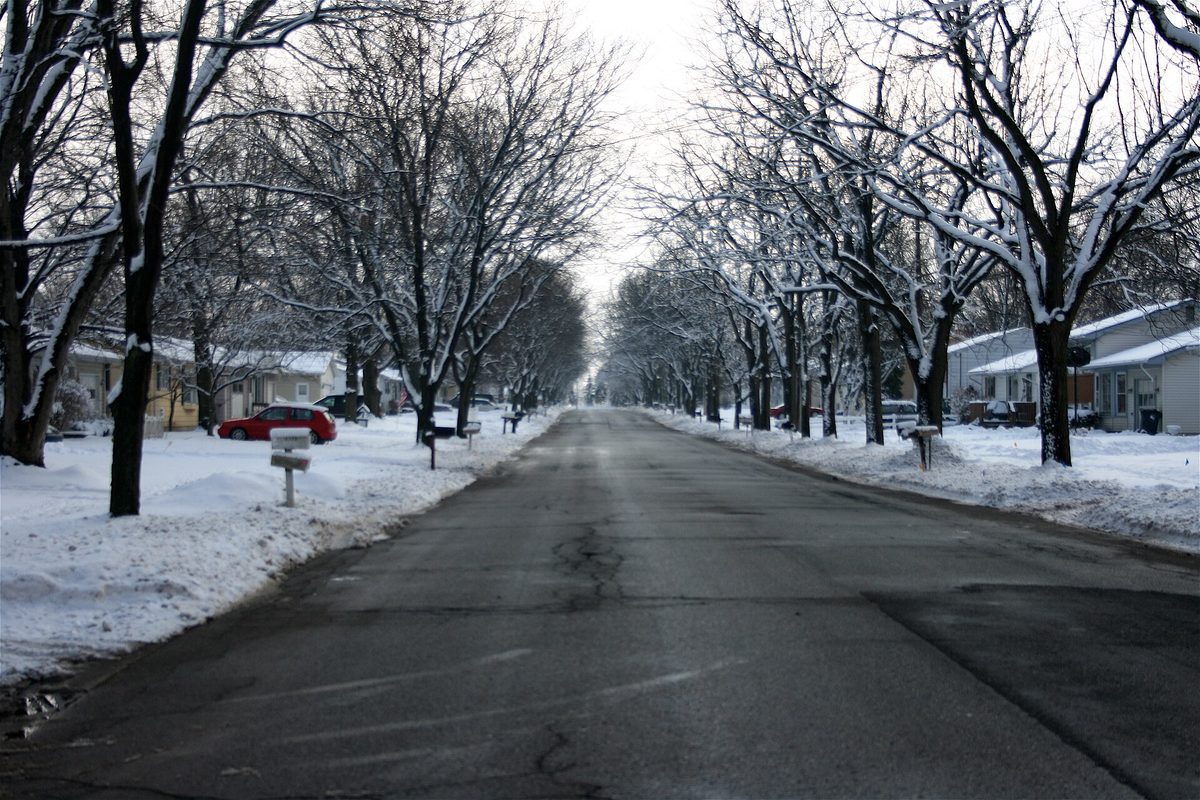 A snow-covered residential street in Portage lined with bare trees, mailboxes at the curb and a red car parked beside a house