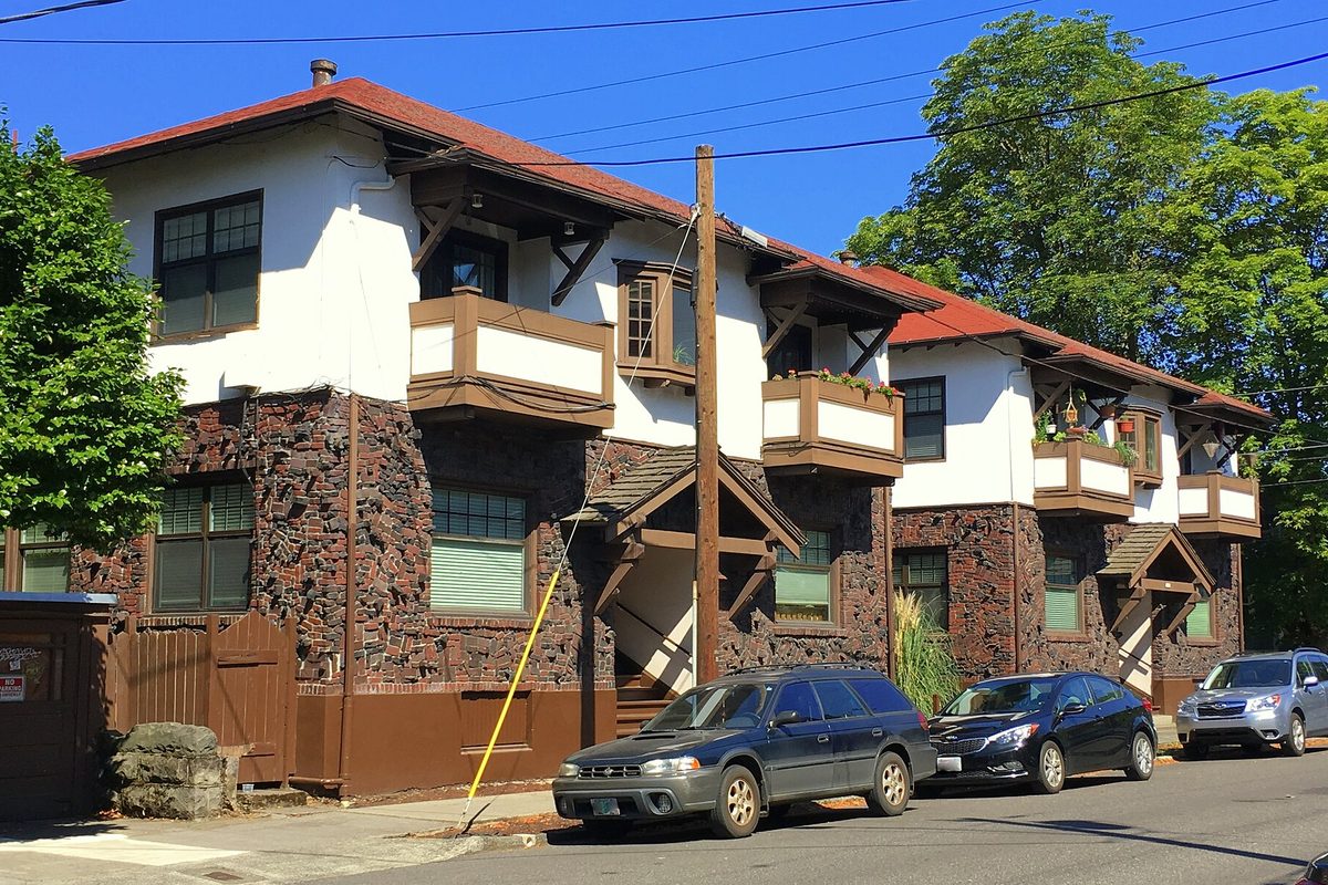 The Irvington Bowman Apartments in Portland, a white stucco and dark stone building with a red tile roof, with cars parked along the street in front