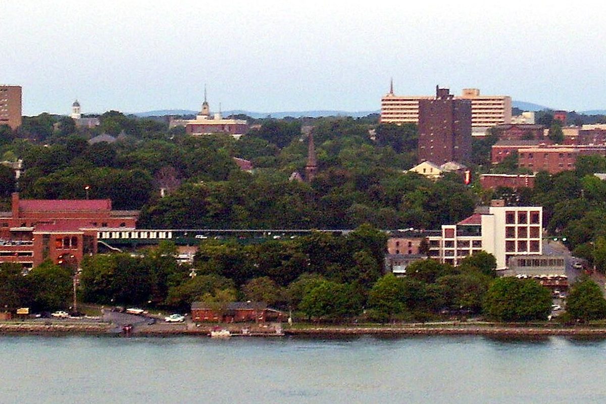 Poughkeepsie seen from across the Hudson River, brick buildings, church spires and taller apartment blocks rising above trees on the waterfront