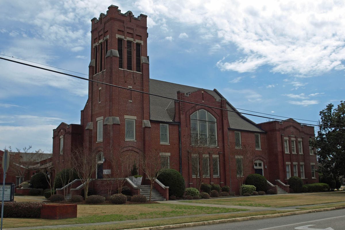 The red brick First Methodist Church of Prattville, with its square bell tower and a large arched window, under a blue sky with clouds