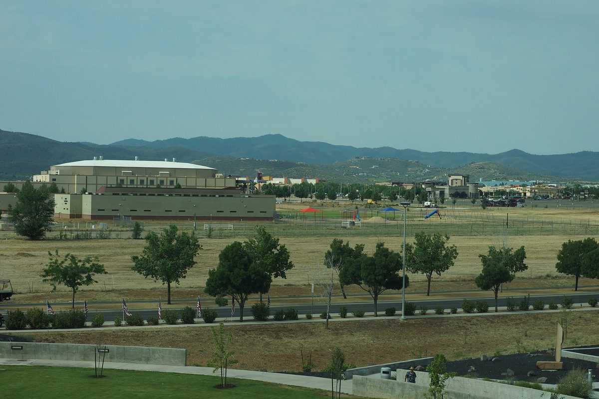 View southwest from the Prescott Valley Civic Center over a grassy field and young trees toward a large white-roofed building and mountains