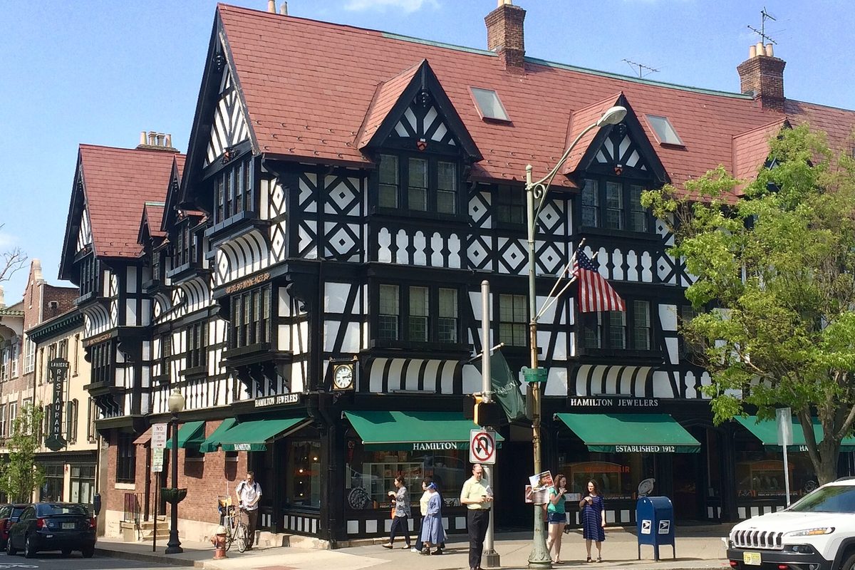 A black-and-white half-timbered Tudor Revival building with a red tile roof and green awnings over Hamilton Jewelers on a sunny Princeton street corner