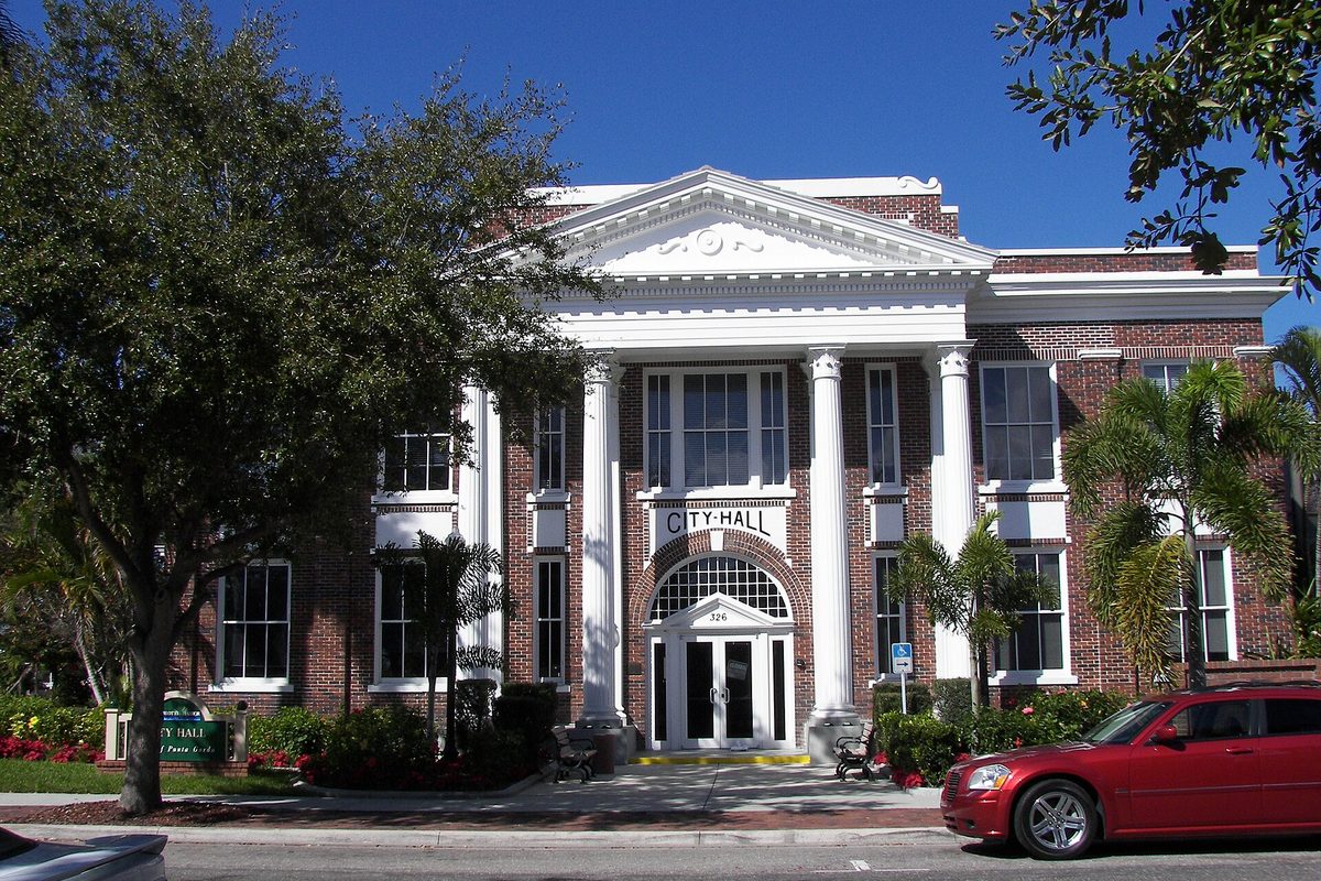 Punta Gorda City Hall, a red brick building with a white columned portico and arched entry, with a red sedan parked at the curb