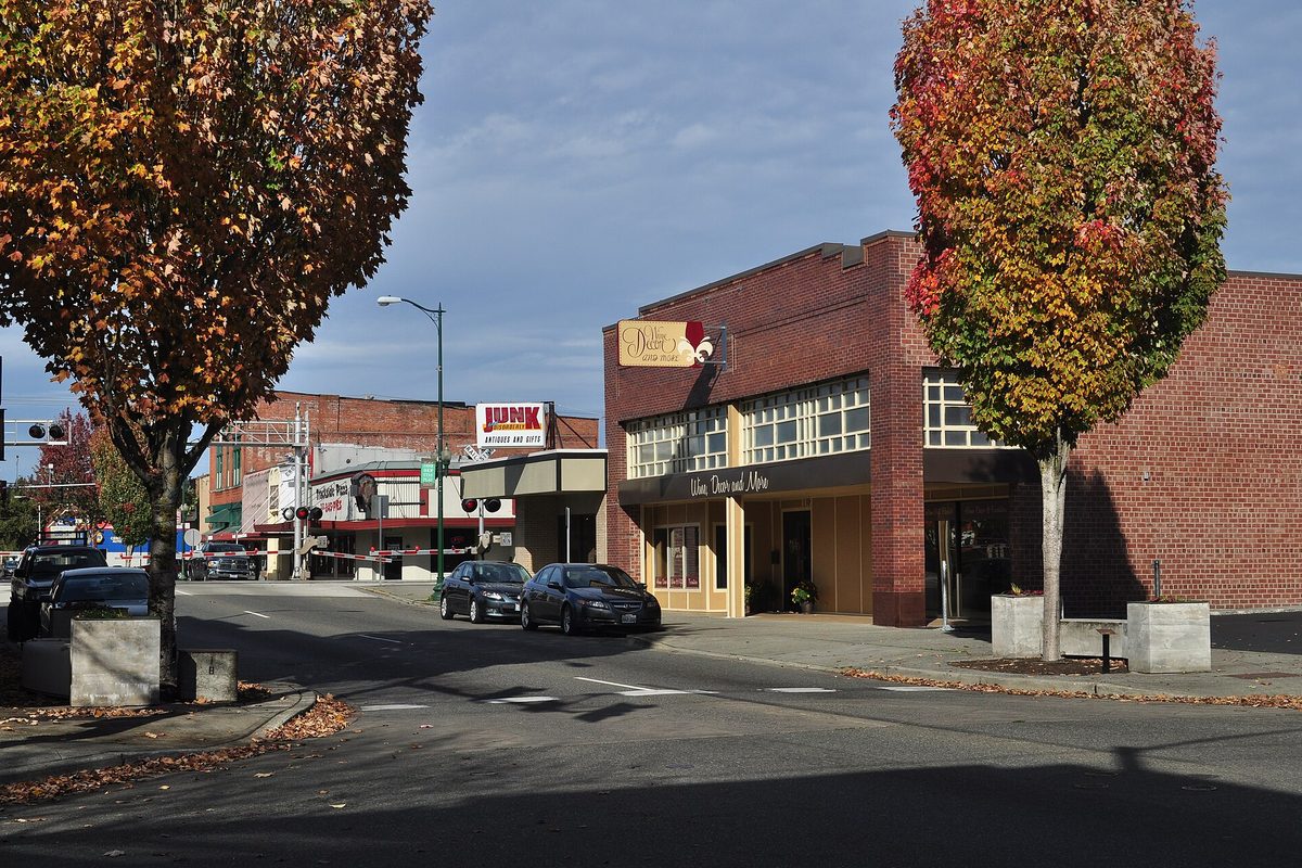 Brick storefronts on North Meridian in downtown Puyallup with autumn-colored trees, parked cars and a railroad crossing signal down the street