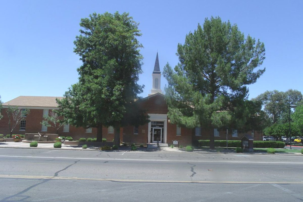 Queen Creek Town Hall, a red brick building with a white steeple, behind two large shade trees on a sunny day
