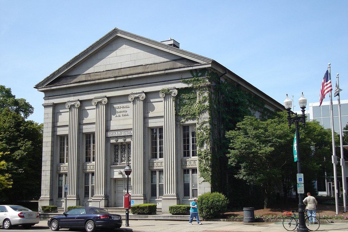 Quincy's 1844 granite town hall with Ionic columns and ivy climbing one side, a dark sedan parked at the curb in front