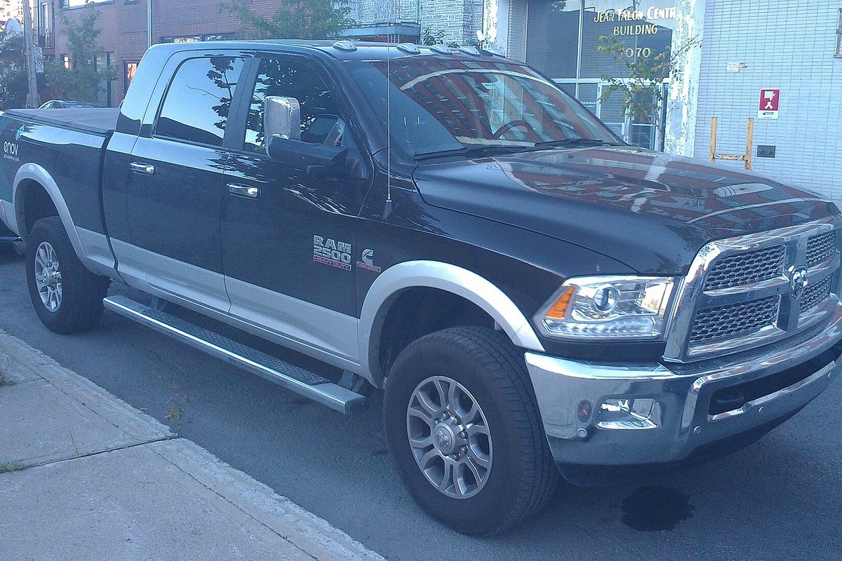 A black and silver two-tone Ram 2500 Heavy Duty four-door pickup with a Cummins badge on the door, parked at a city curb