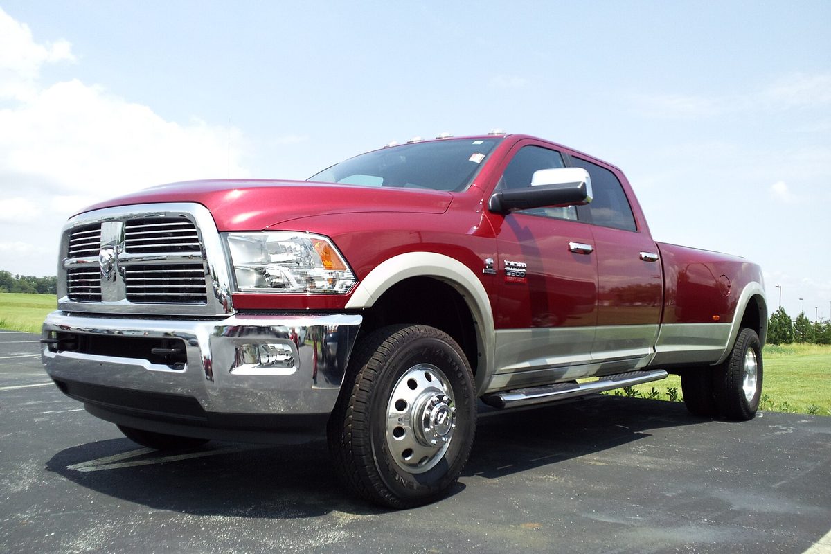 A red Ram 3500 crew cab dually with silver lower trim, chrome grille and dual rear wheels, parked on asphalt under a blue sky