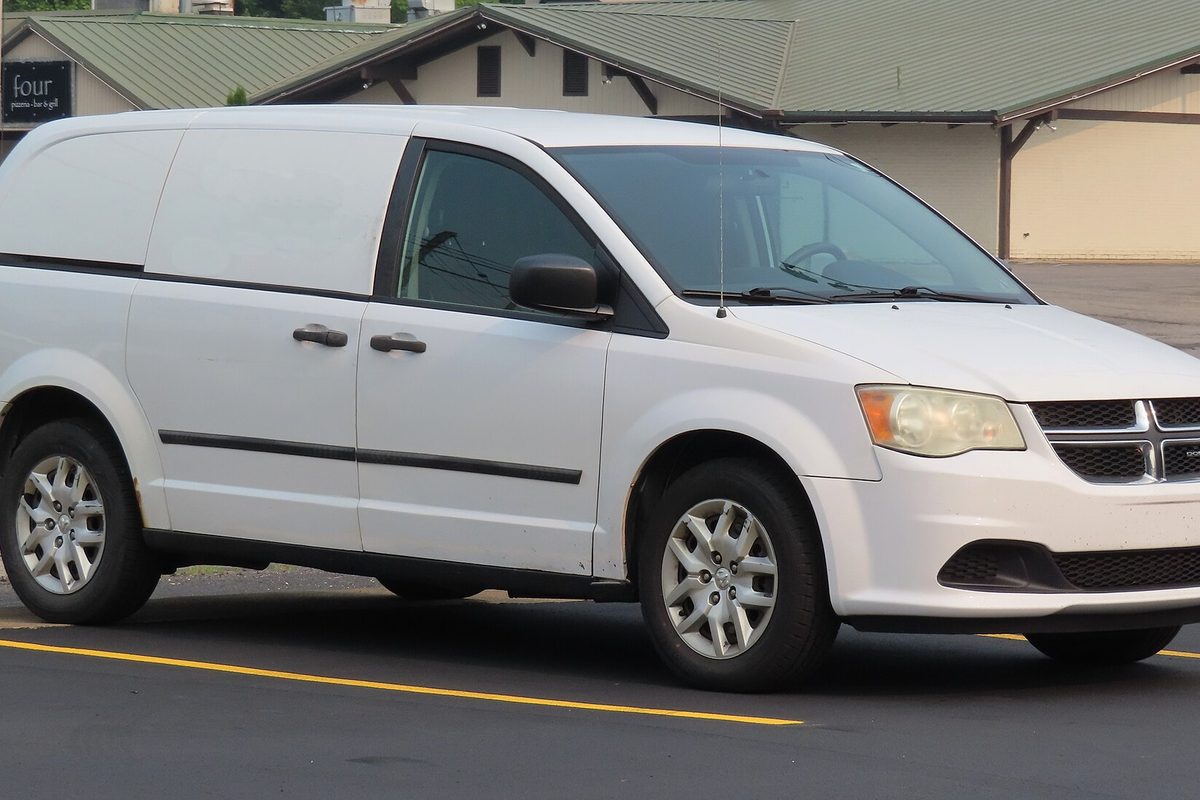 A white 2014 Ram C/V Tradesman cargo minivan with solid panels in place of rear side windows, parked in a lot