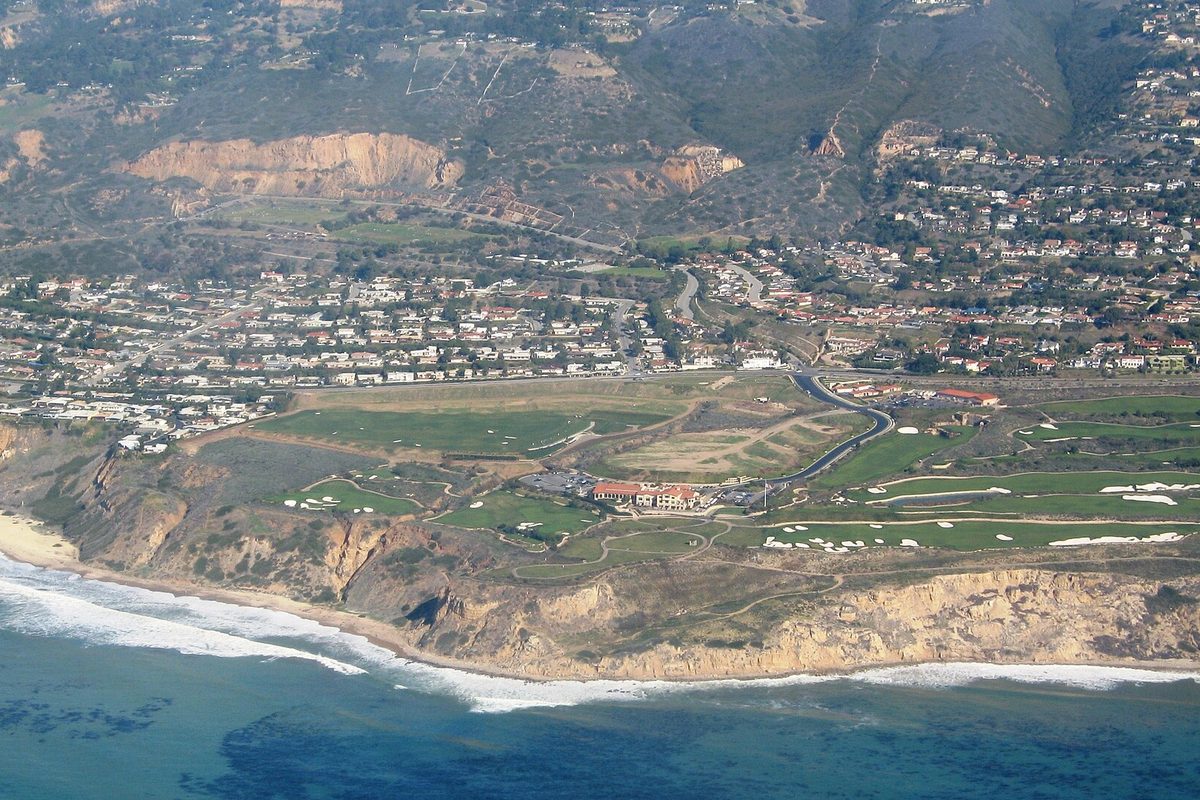 Aerial view of a clifftop golf course above the Pacific in Rancho Palos Verdes, with hillside neighborhoods rising behind it