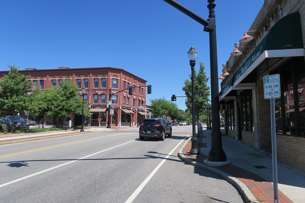 Main Street in Reading on a sunny day, with a red brick corner building hung with flag bunting, black street lamps and a dark SUV in the lane