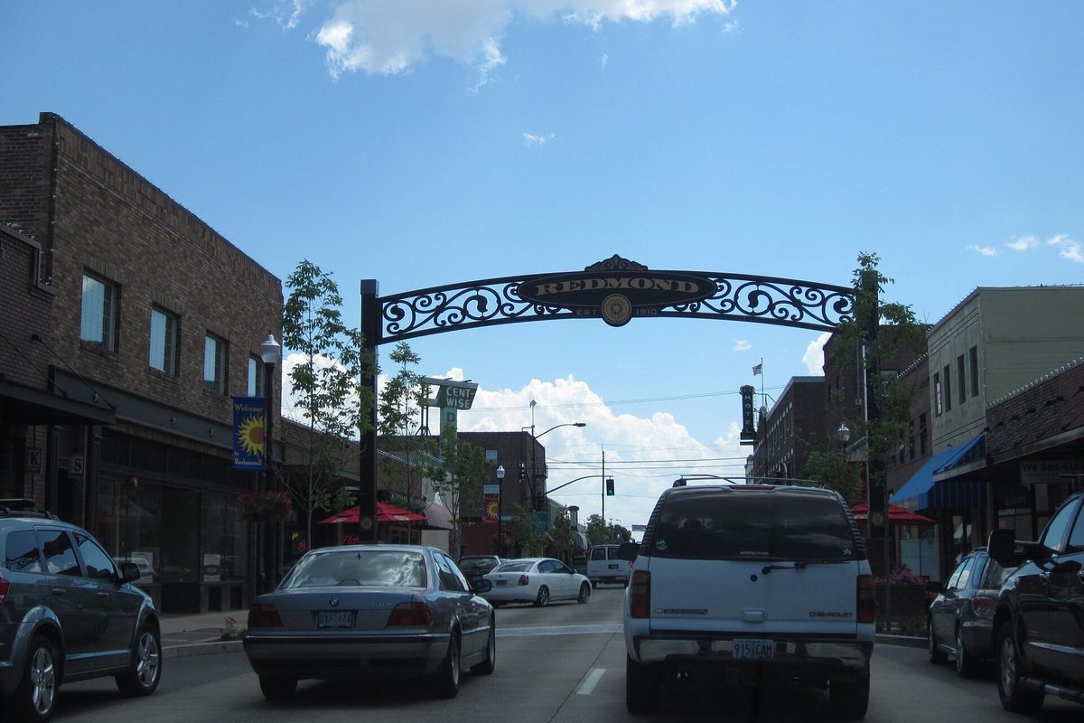 A wrought-iron arch reading Redmond spans a downtown street lined with brick buildings, with cars driving underneath
