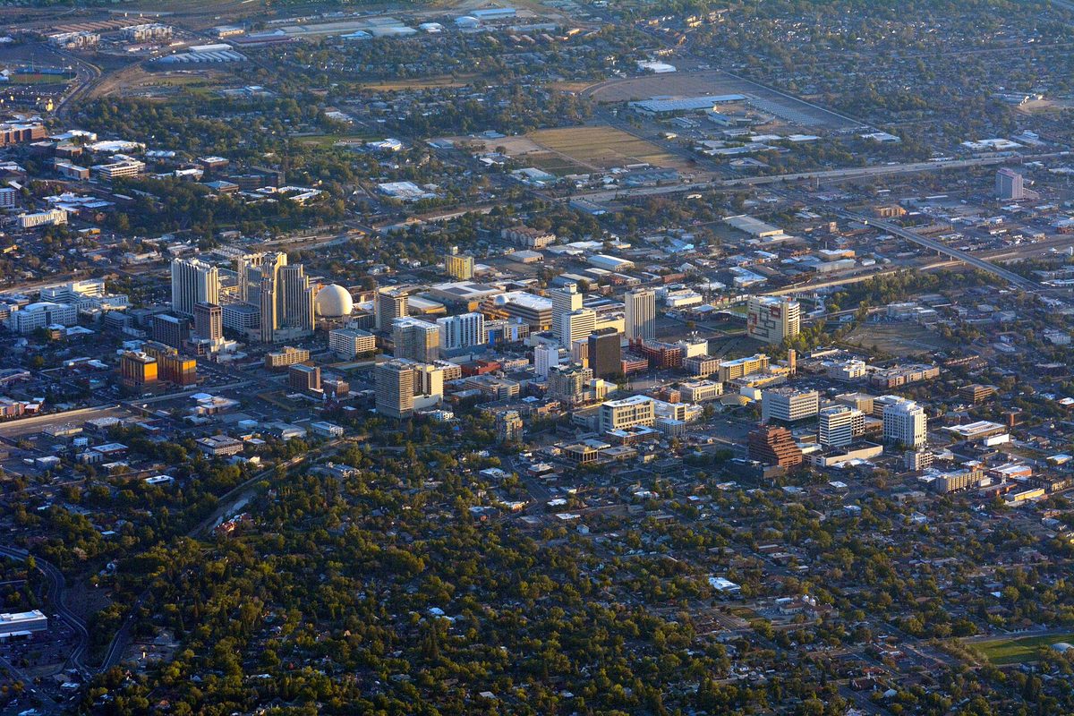 Aerial view of downtown Reno at golden hour, with a cluster of high-rise hotels and a domed building rising above tree-filled neighborhoods