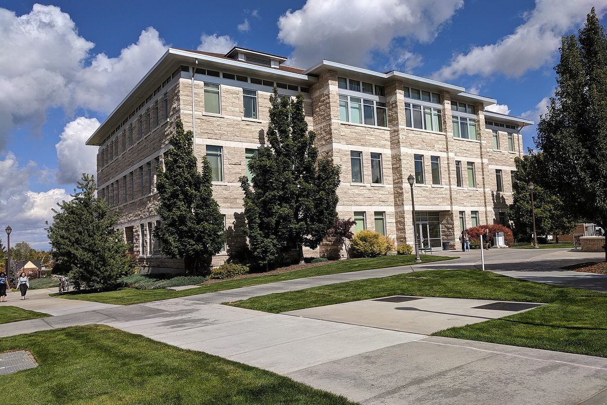 The four-story stone and glass Jacob Spori Building on the BYU-Idaho campus in Rexburg, with lawns, walkways and evergreen trees