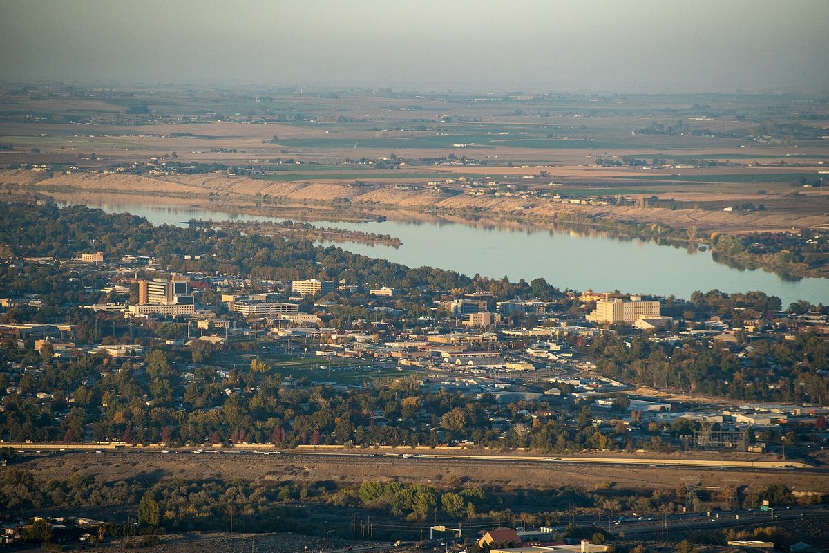 Aerial view of downtown Richland at golden hour, with low buildings and trees beside the Columbia River and farmland beyond